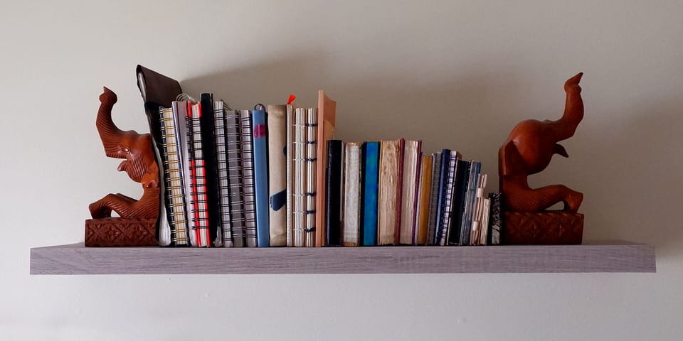 Shelf holding a variety of sketchbooks from big to small with wooden elephant bookends.